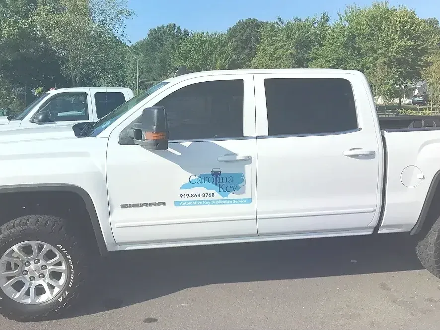 A white truck is parked in a parking lot with trees in the background.
