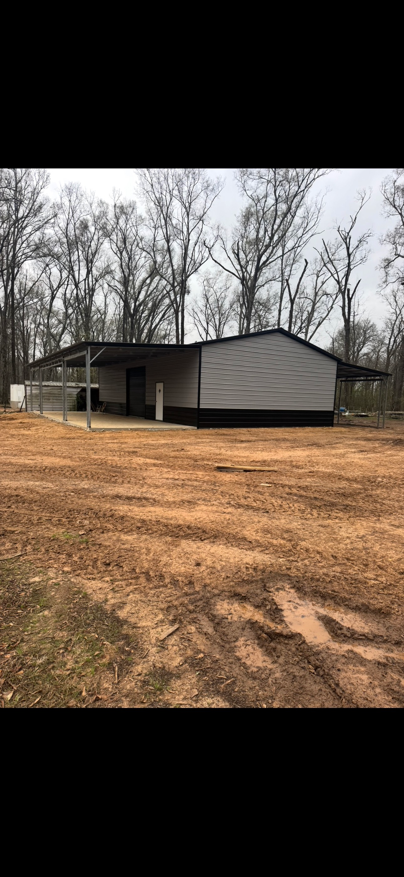 A house is sitting in the middle of a dirt field surrounded by trees.