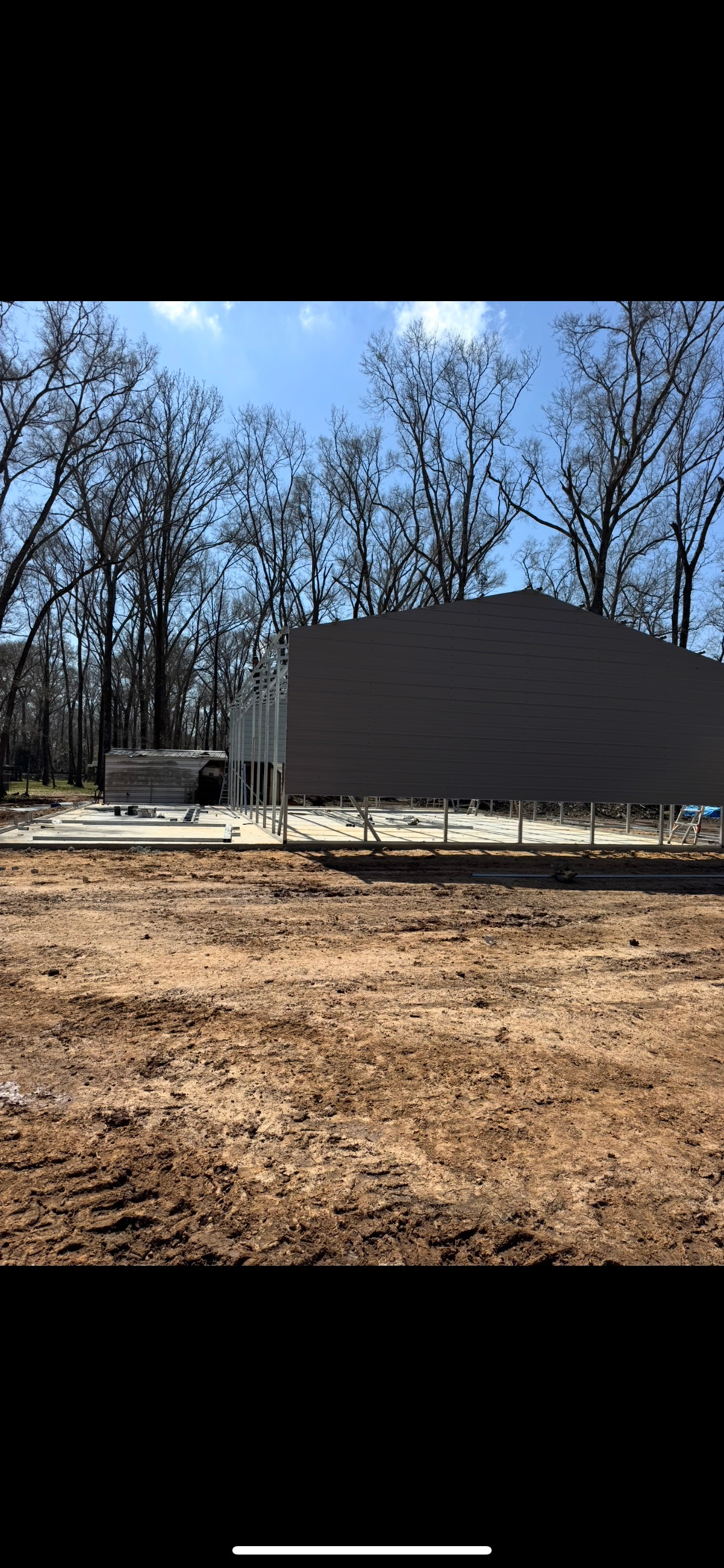 A large dirt field with a house in the background and trees in the background.