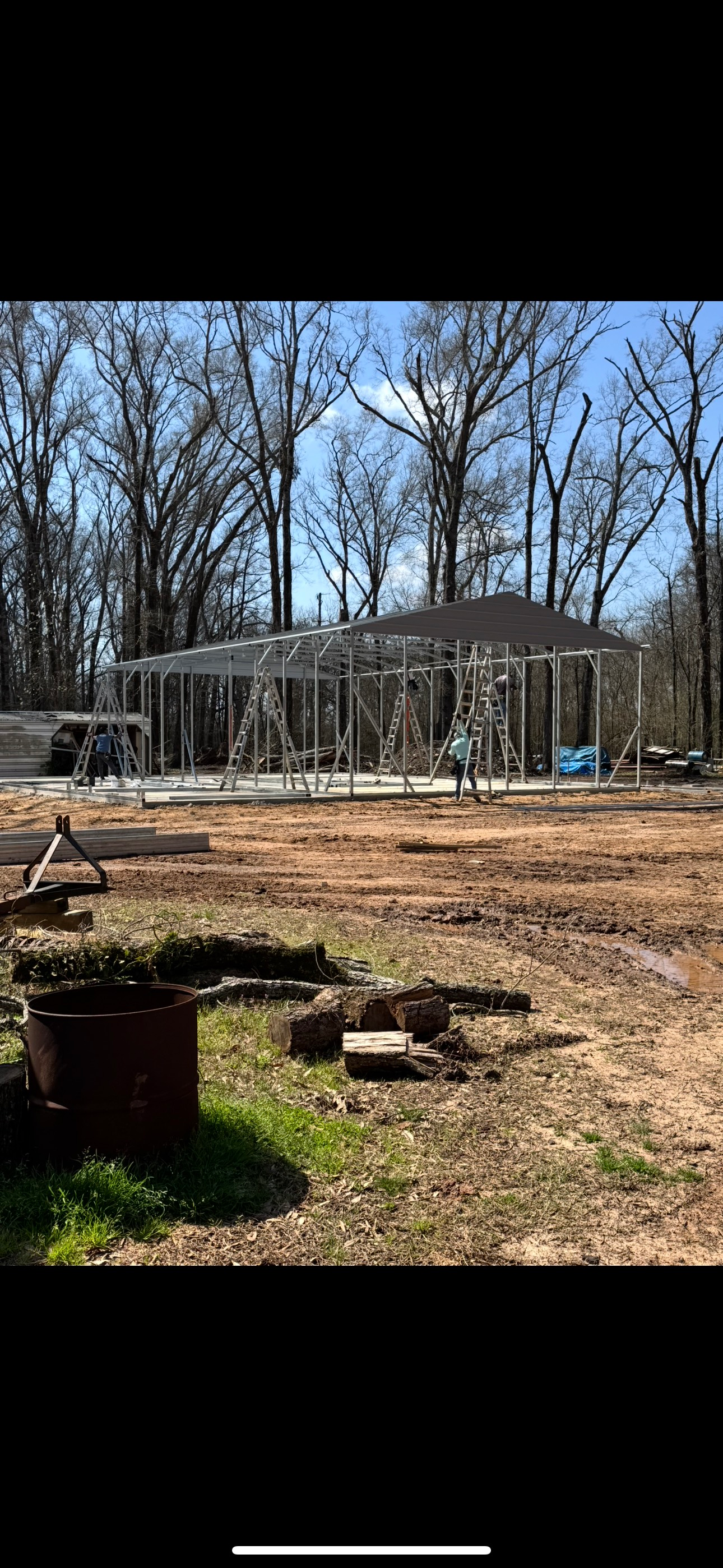 A house is being built in the middle of a dirt field surrounded by trees.