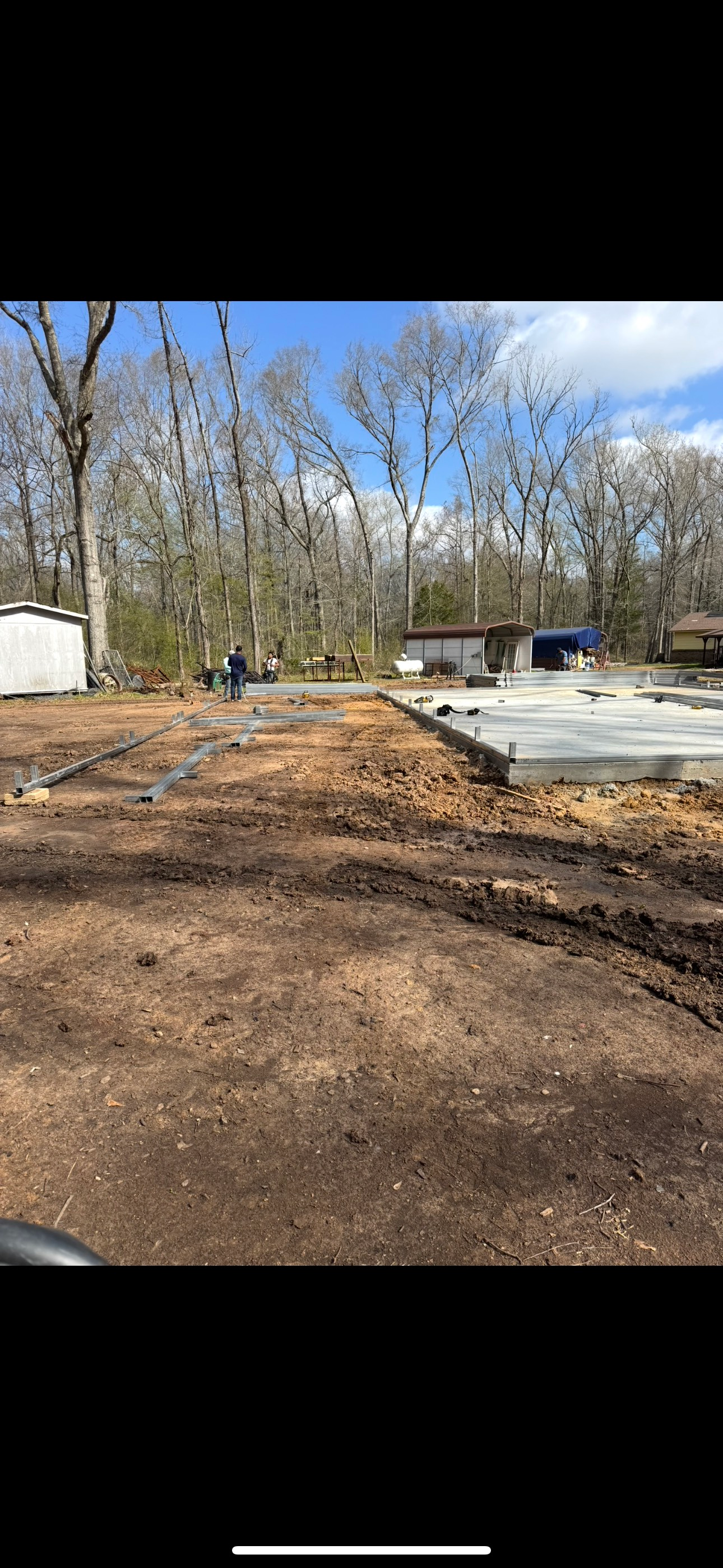 A dirt field with a house in the background and trees in the background.