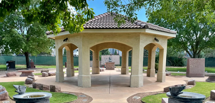 Rendering of a memorial with a central cross and surrounding structures, trees, and sky.