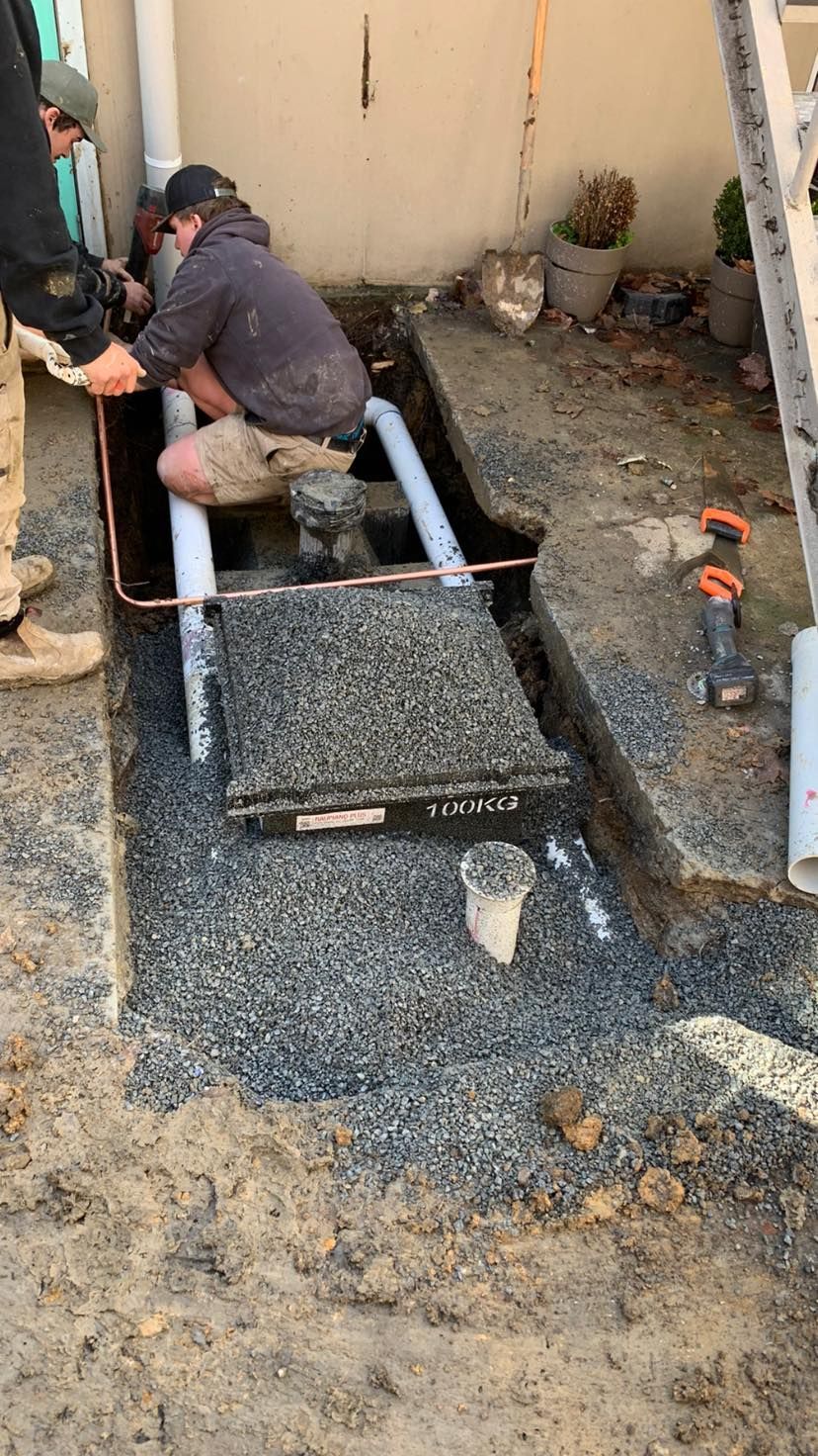 Two people working on plumbing in a gravel trench. Flushed Away Plumbing in Bowral