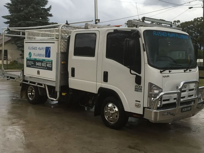 Three Flushed Away Plumbing trucks parked in a grassy field with trees in background.
