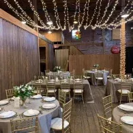 Elegant indoor banquet setup with gold chairs, white table settings, and string lights overhead