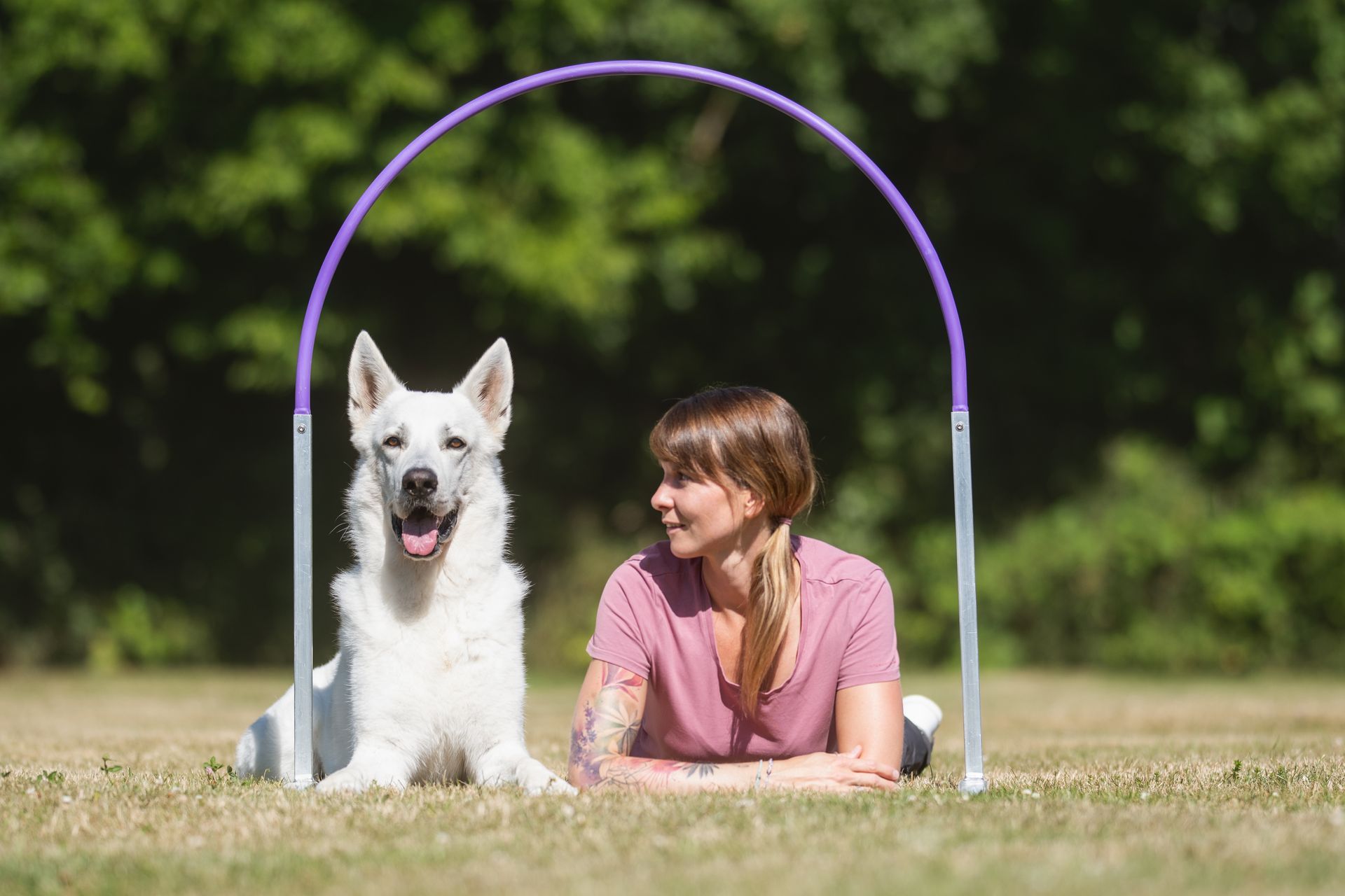 Ramona Houscht und weißer Schäferhund Jimmy liegen in der Wiese unter einem Hoop