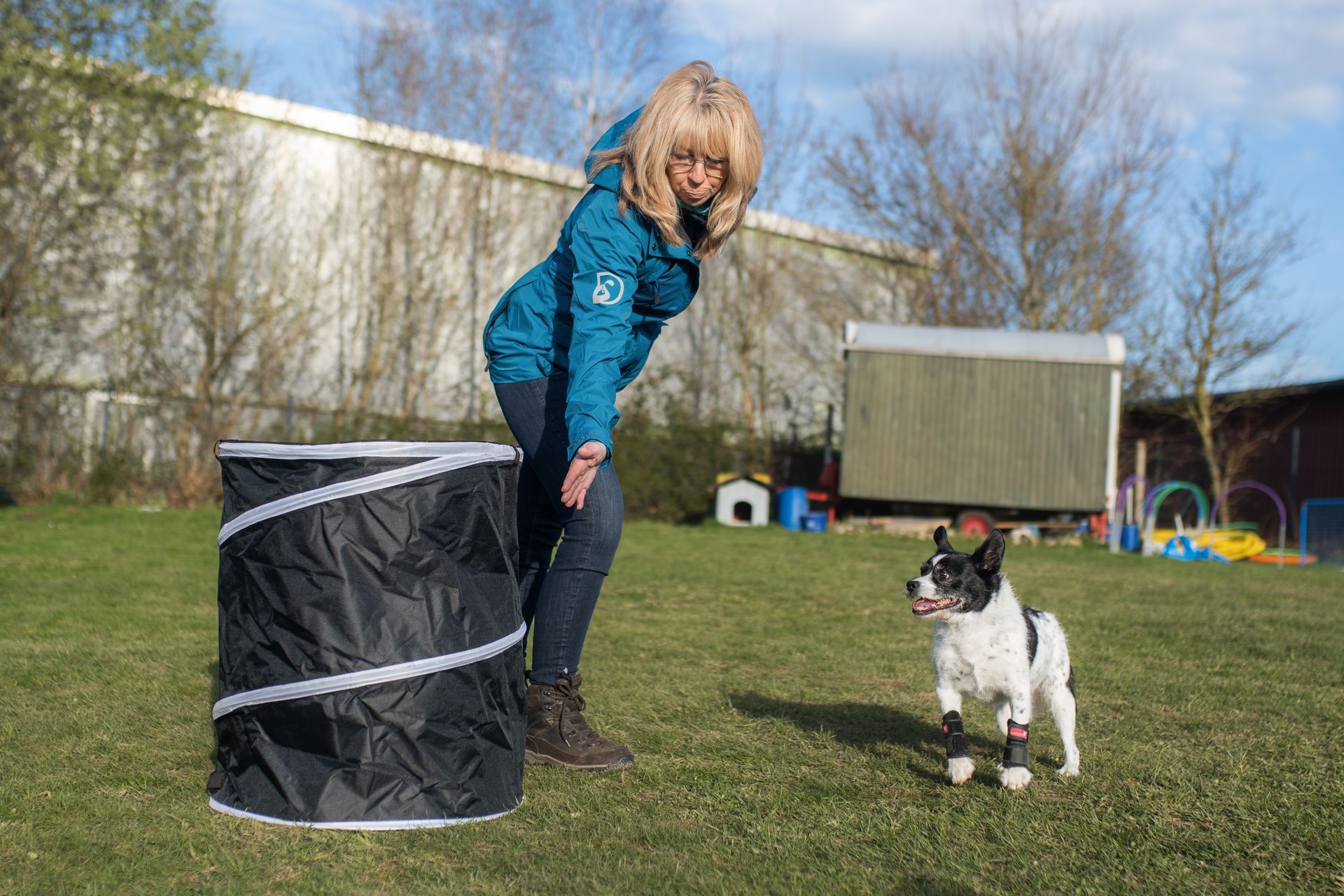 Frau mit ihrem Hund im Hoopers Parcours, Hund geht um eine Hoopers Tonne