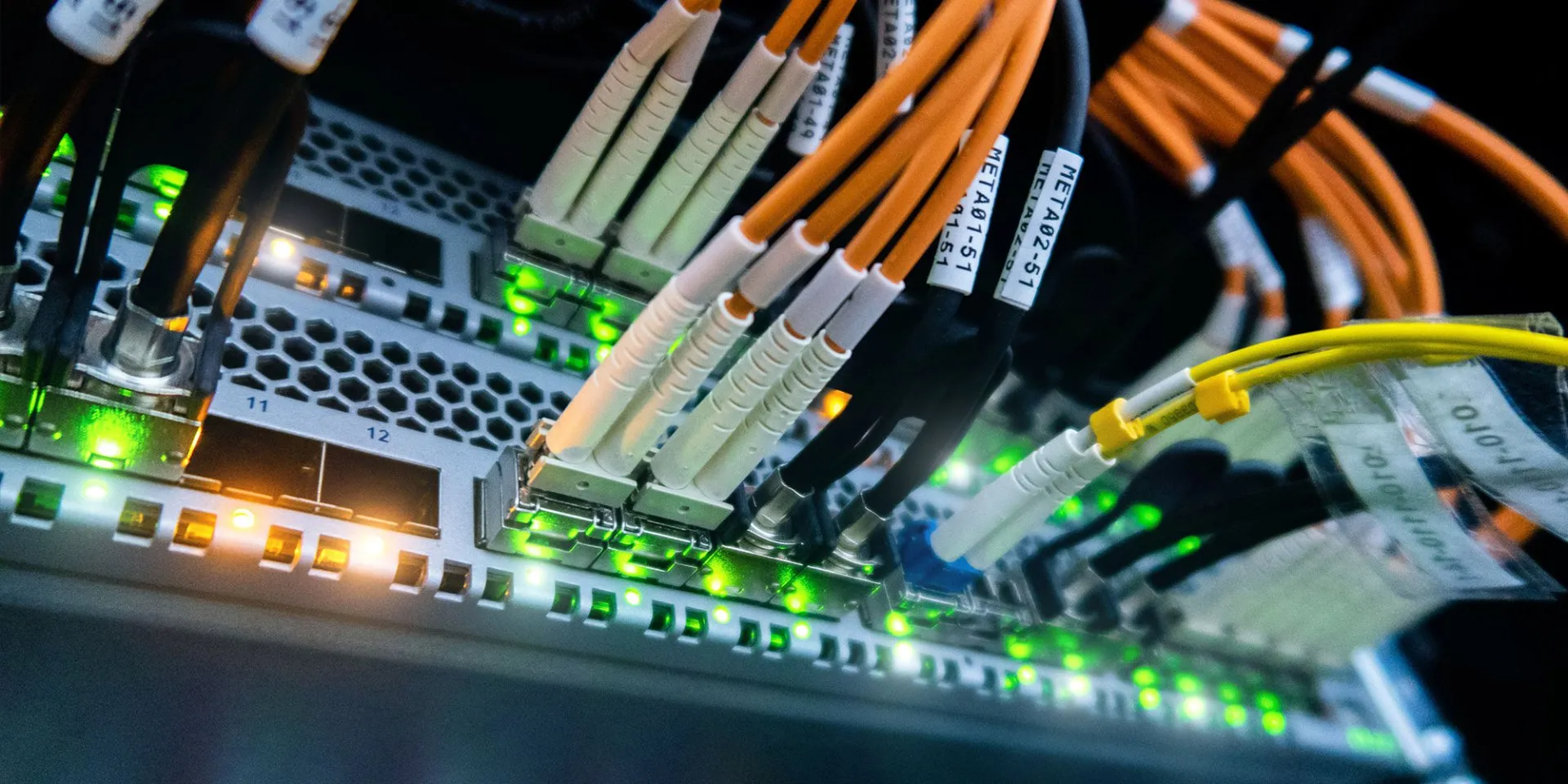 Close-up of network switch ports with orange and yellow Ethernet cables and green indicator lights