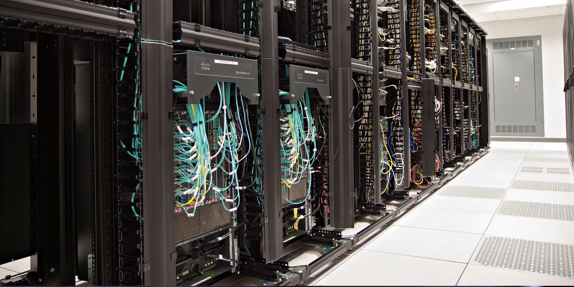 Row of server racks in a data center corridor with cables and equipment lights