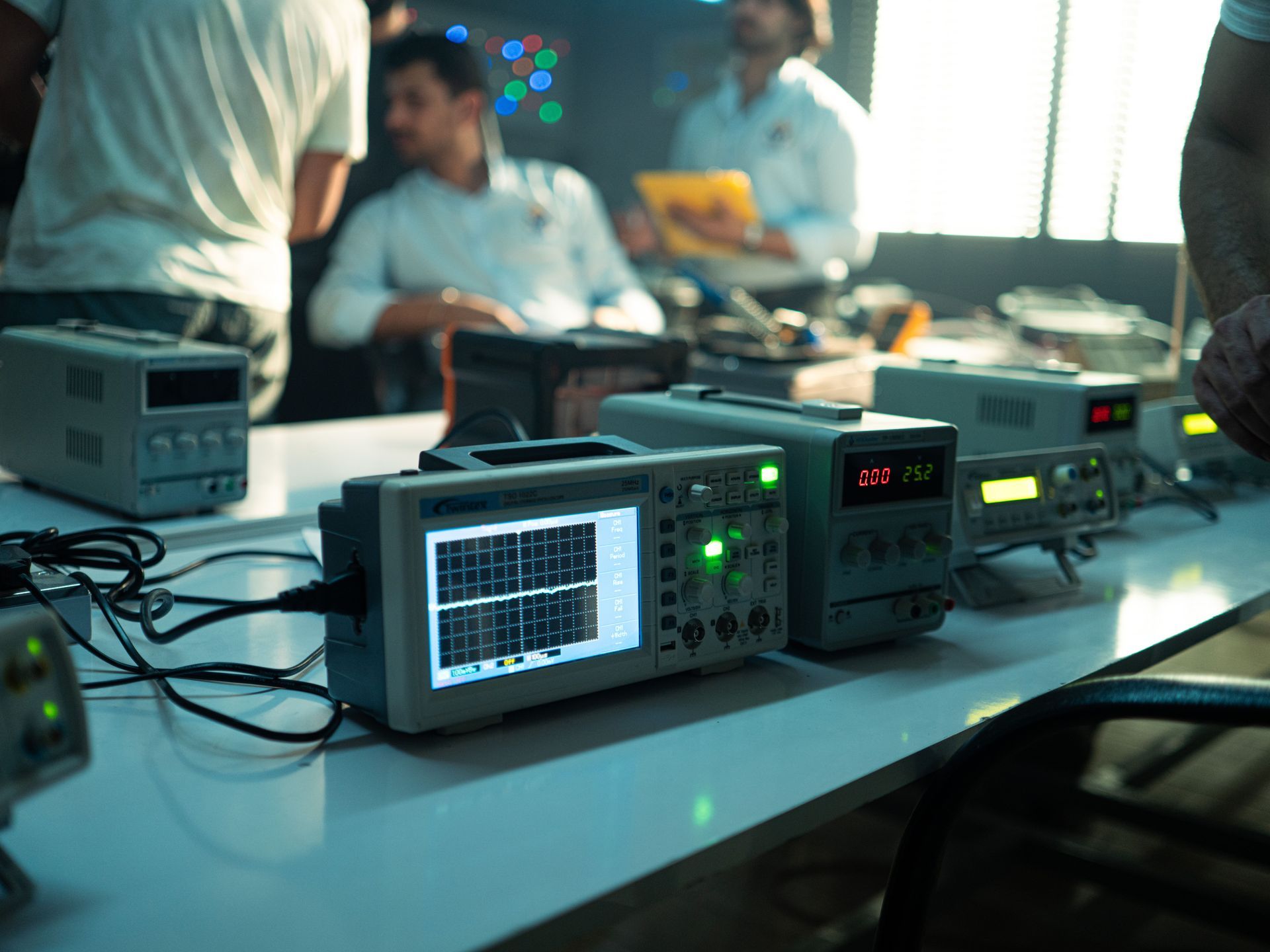 Electronic test equipment on a table with people working in the background