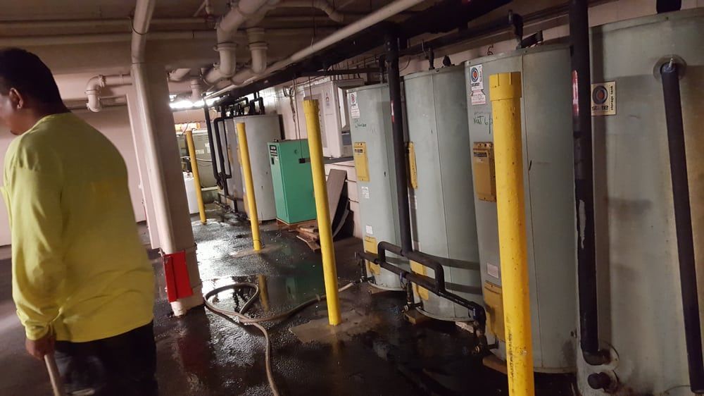 A man is standing in a room with water heaters and pipes.