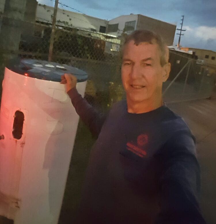 A man in a blue shirt is standing next to a water heater