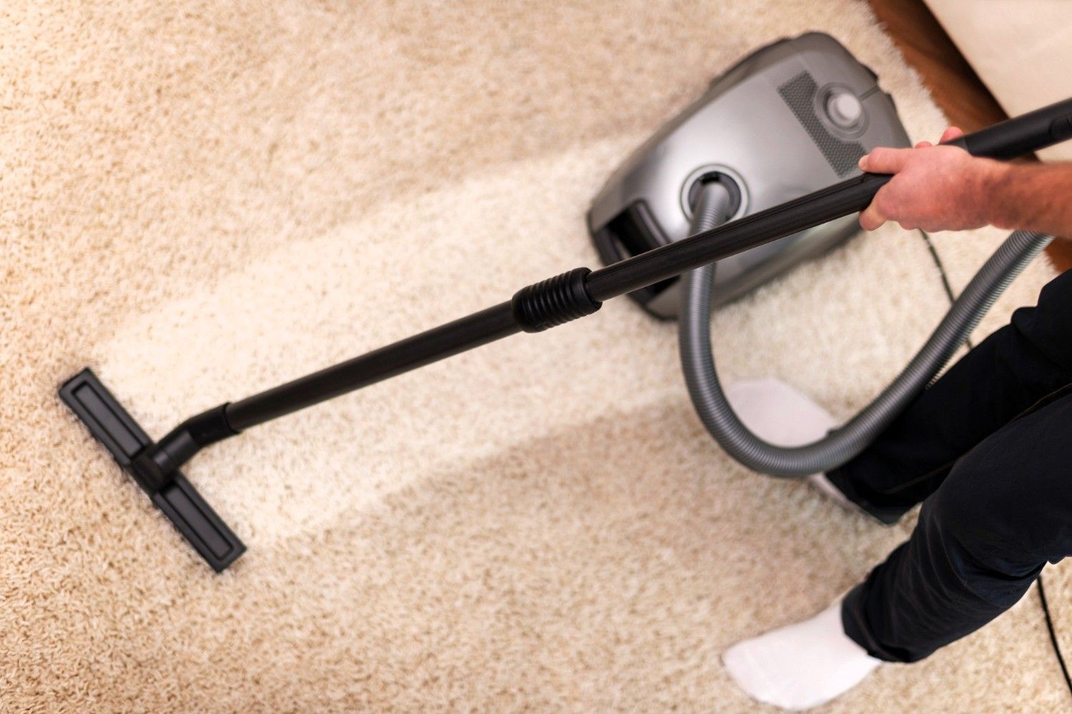 Person vacuuming light carpet with gray vacuum cleaner