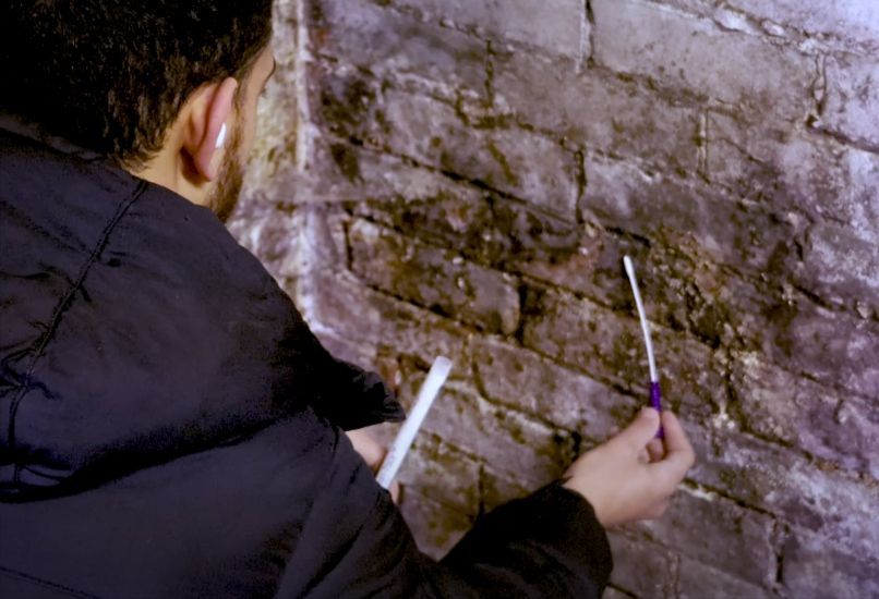 A homeowner is kneeling down to conduct a mold inspection