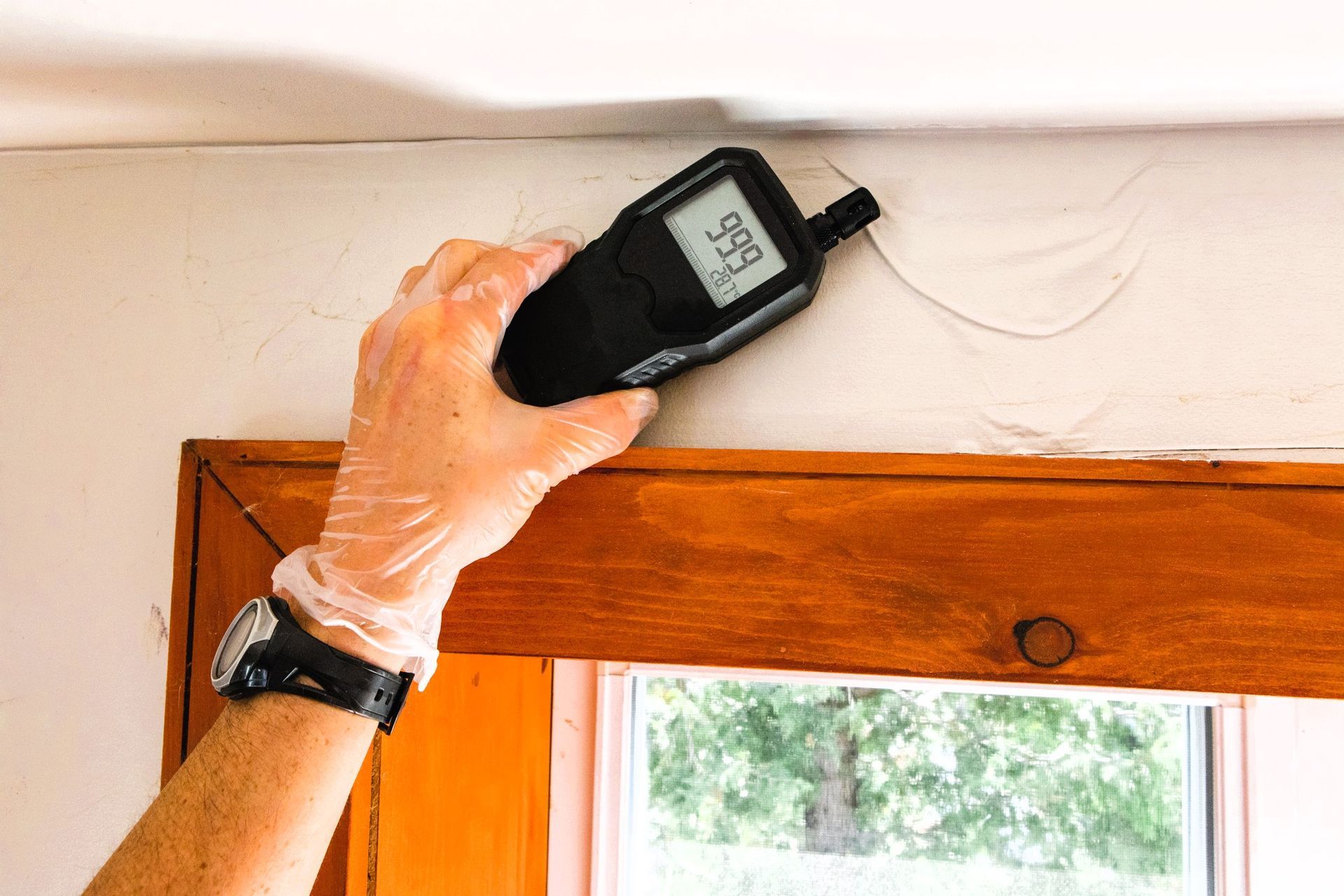 Hand holding moisture meter against wall showing 9.9% reading