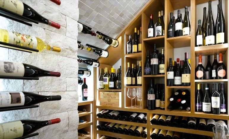 Rows of various wine bottles on wooden shelves inside a wine cellar.