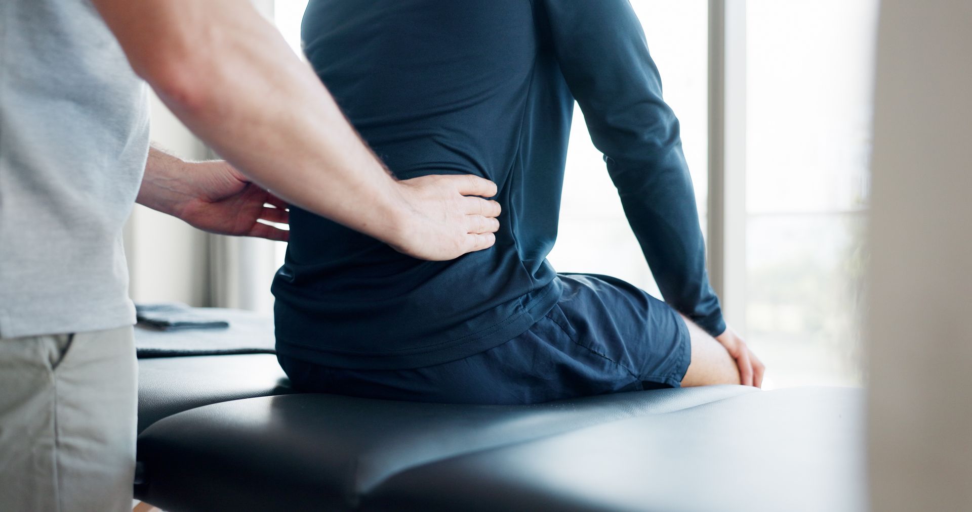 A chiropractor assessing a person's back while seated on an examination table.