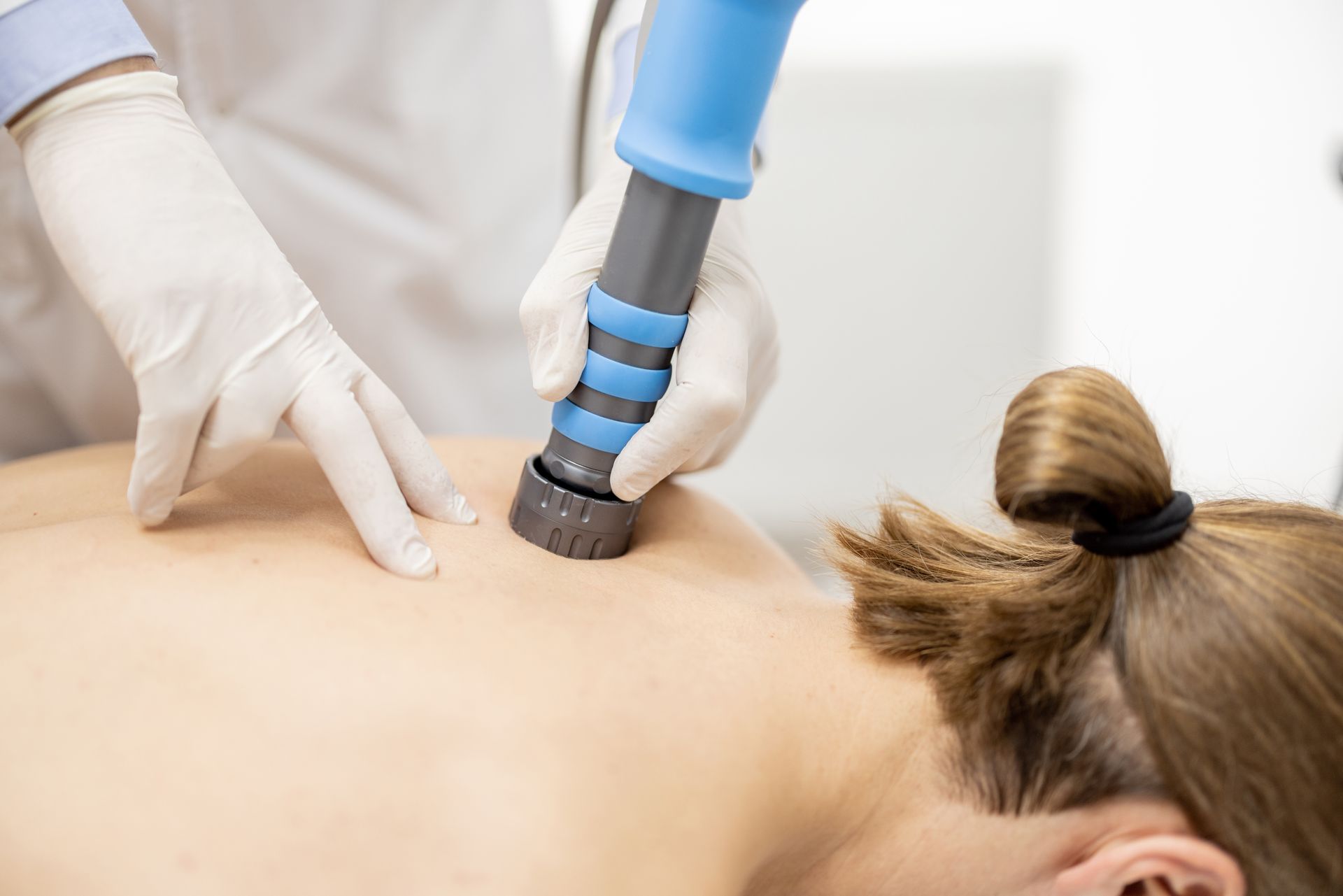 A chiropractor using a blue and gray shockwave on a patient's back during a treatment.