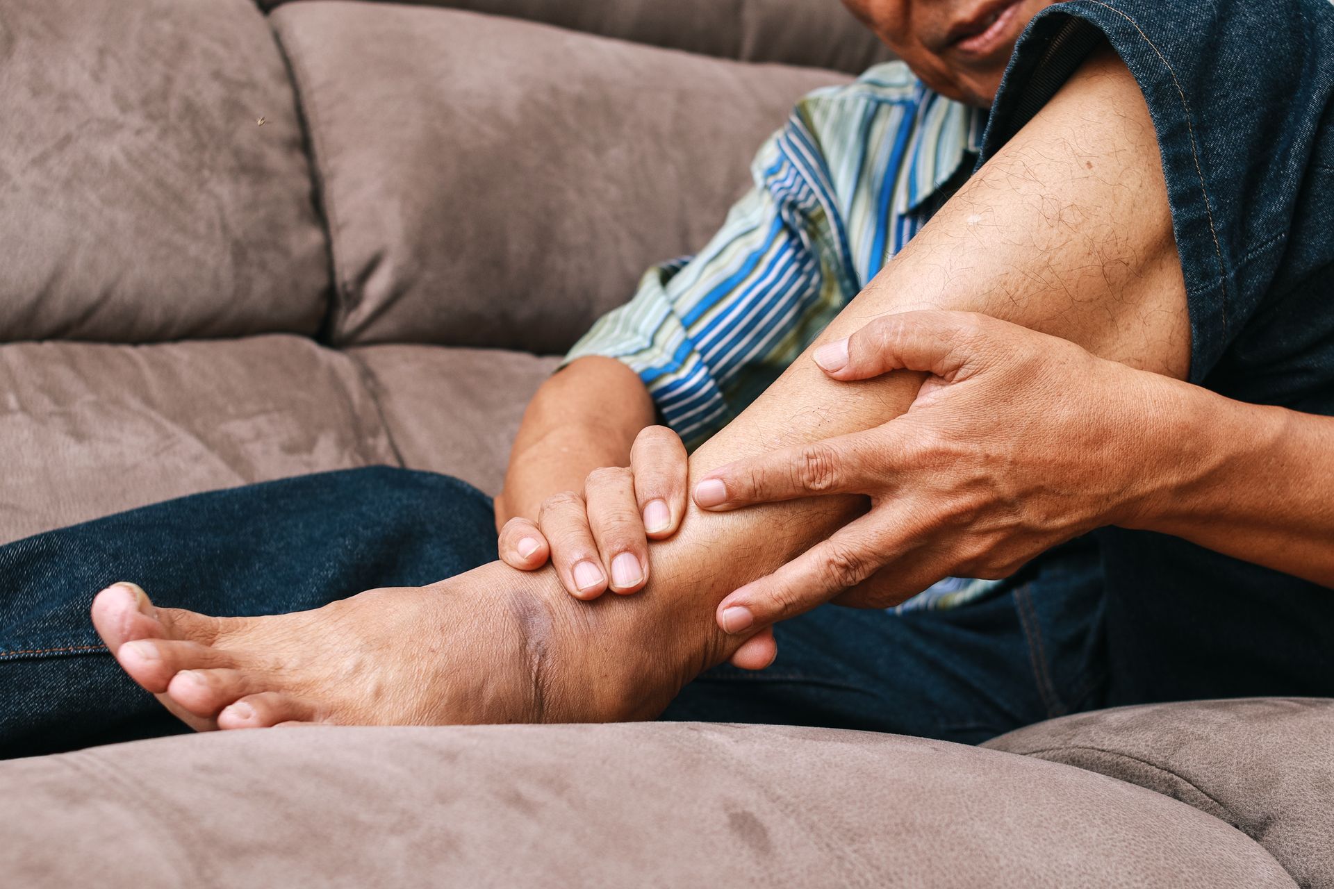 Person seated on a couch, holding their leg. The leg appears swollen, possibly due to a medical condition.