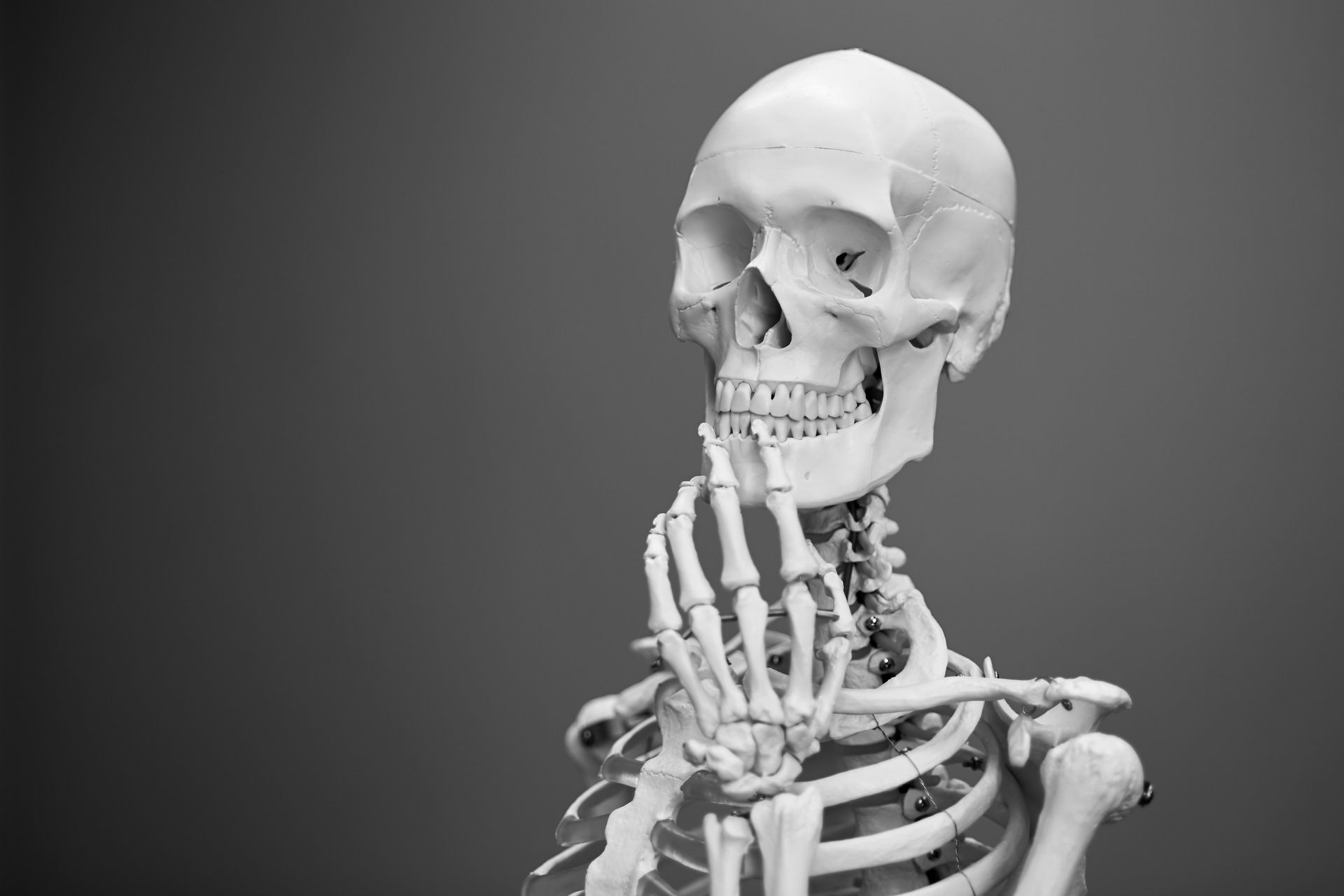 Skeleton figure with hand near mouth, appearing thoughtful, set against a dark background.