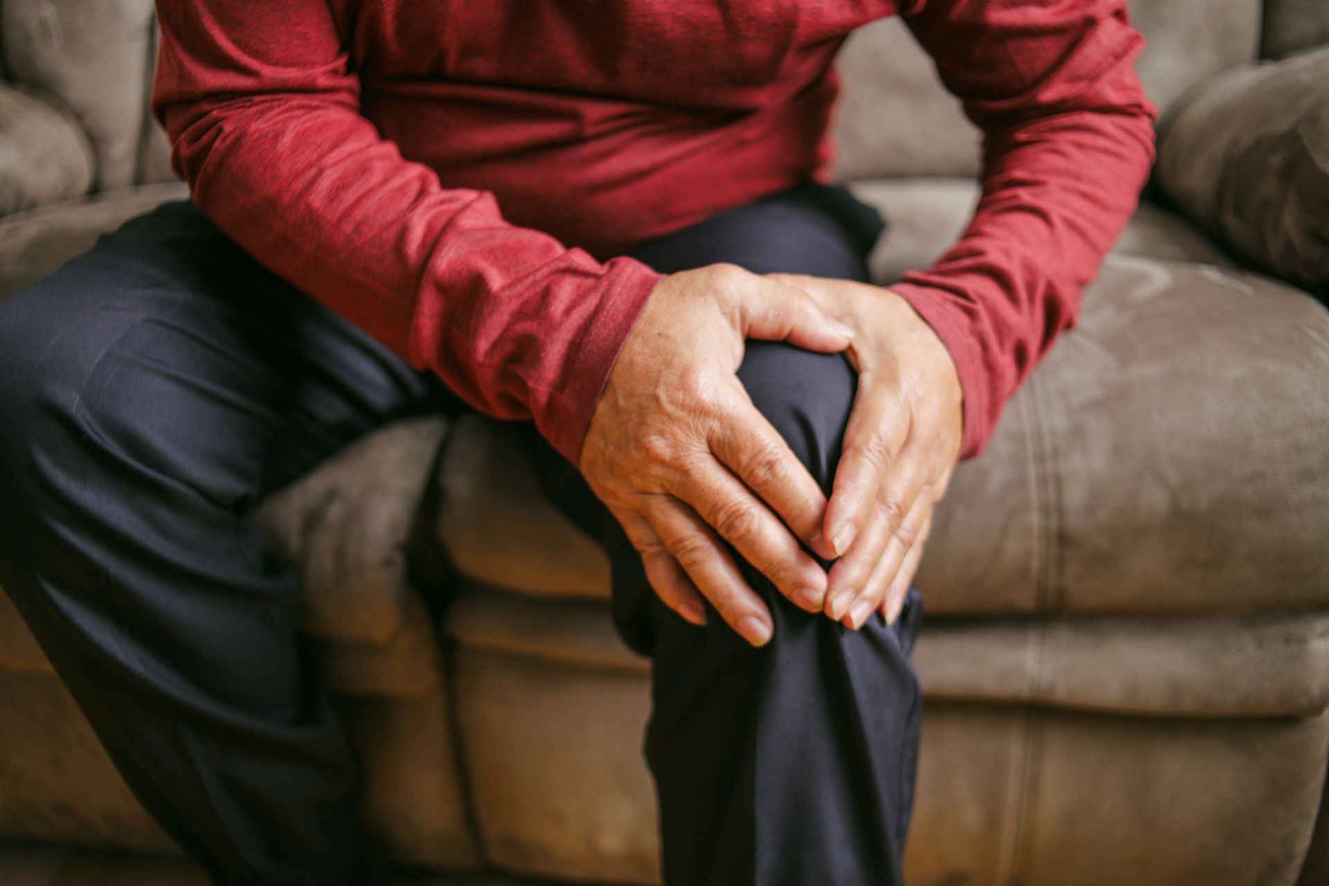 Person holding their hands on their knee, showing signs of pain, indoors.
