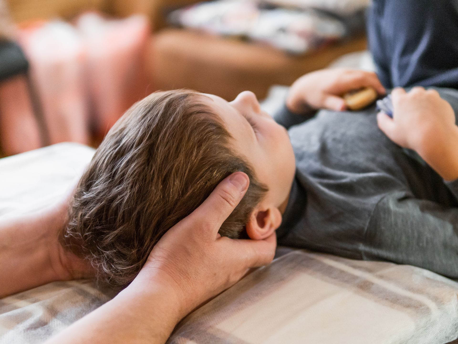 Hands holding a child's head during a chiropractic adjustment on a patterned surface; a person lying down.