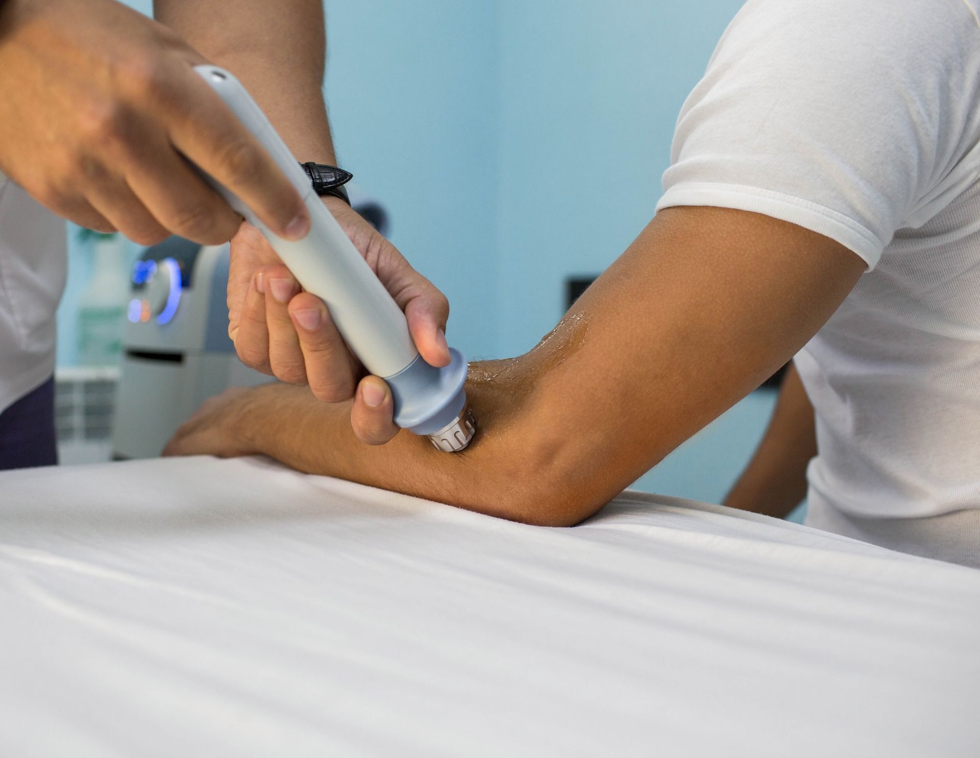 A chiropractor using a shockwave therapy device on a patient's elbow.