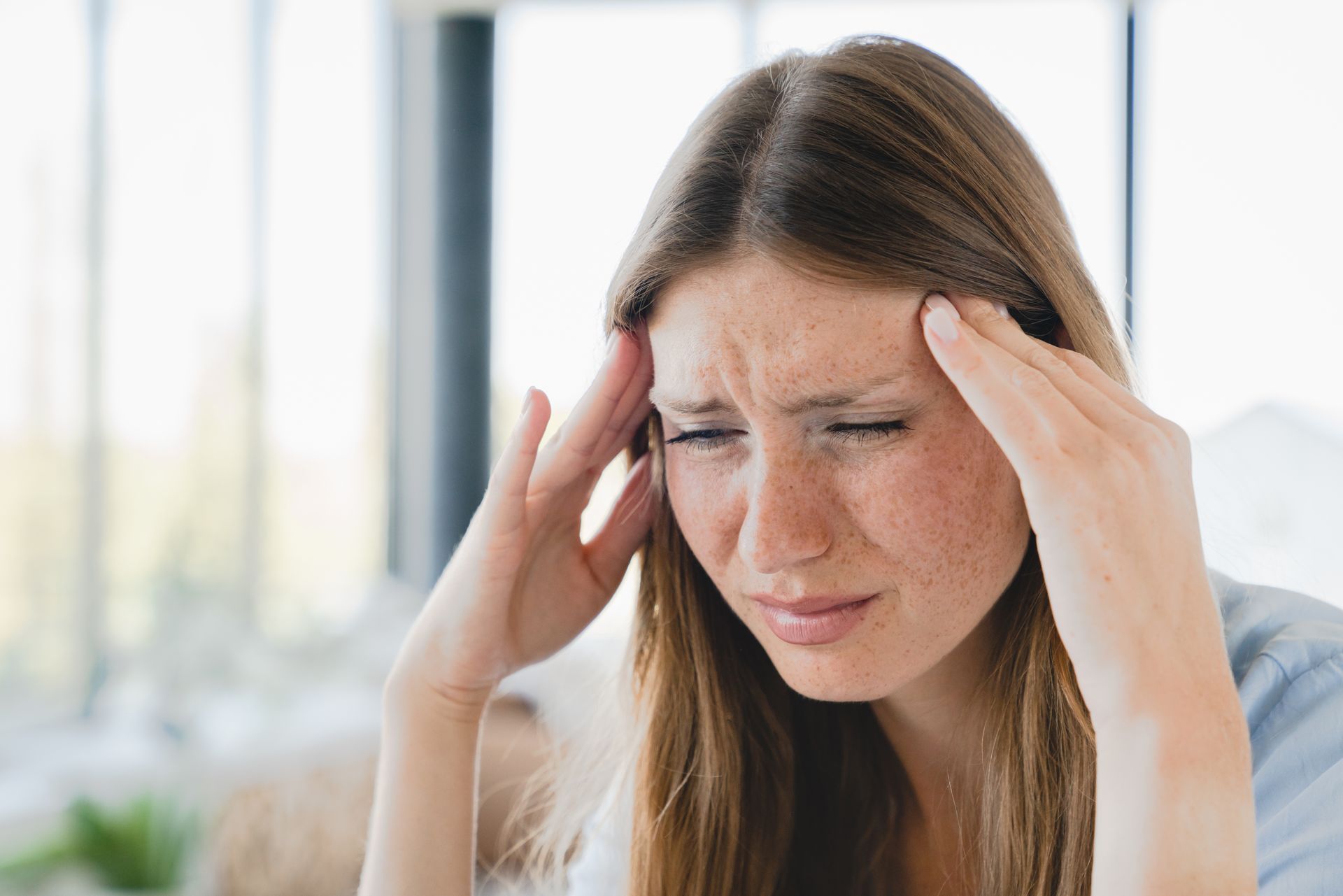 Woman with a pained expression, holding her temples, indoors with natural light.