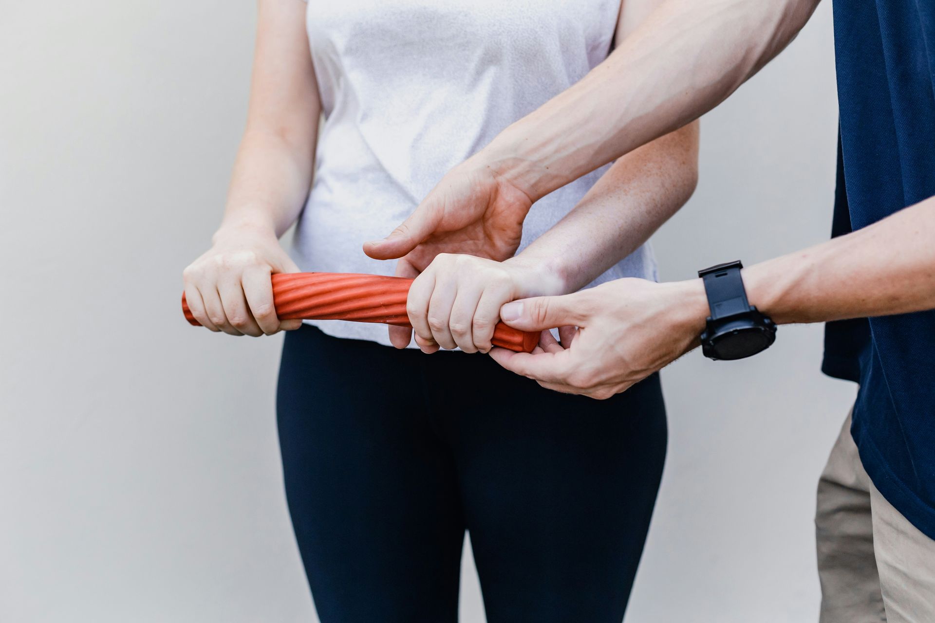 Person holding a red exercise roller, assisted by another person's hands, likely for physical therapy.
