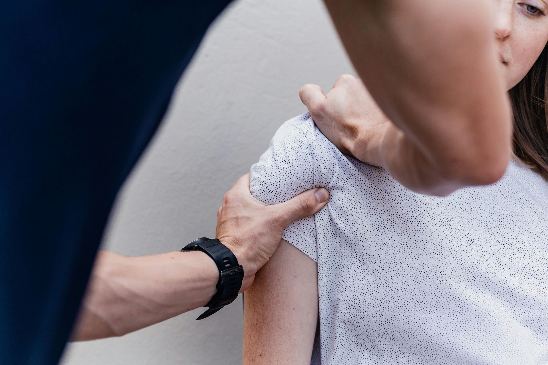 Person's shoulder being examined by a chiropractor; white shirt, dark watch.