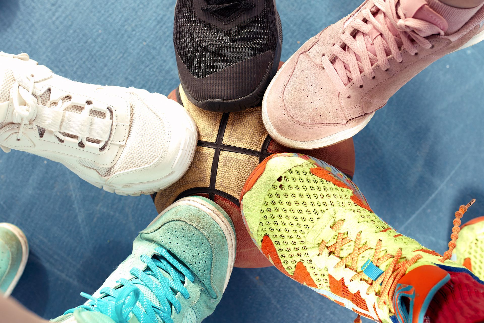 Feet wearing colorful sneakers surround a basketball on a blue court.