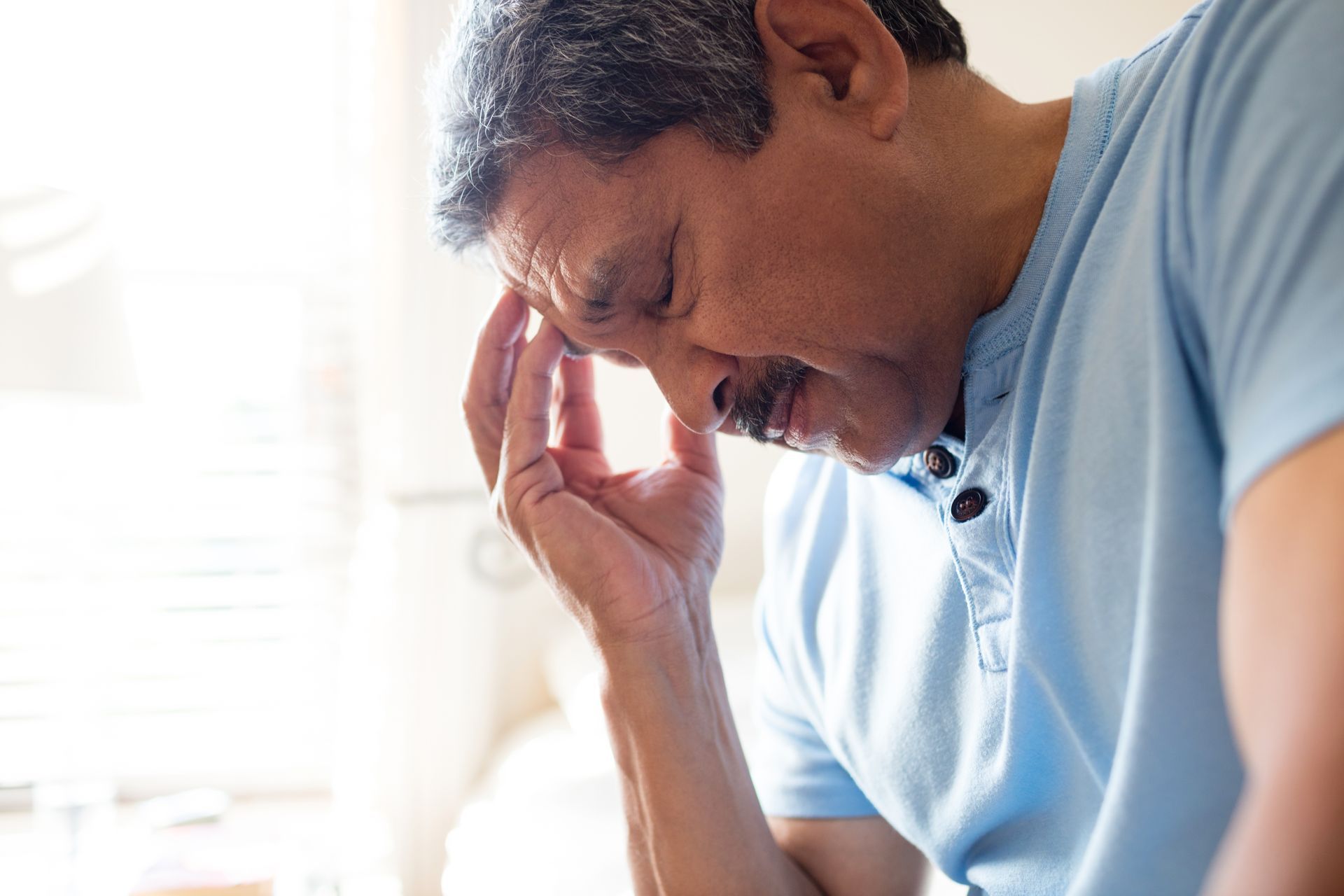 Man holding his head, eyes closed, possibly in pain.