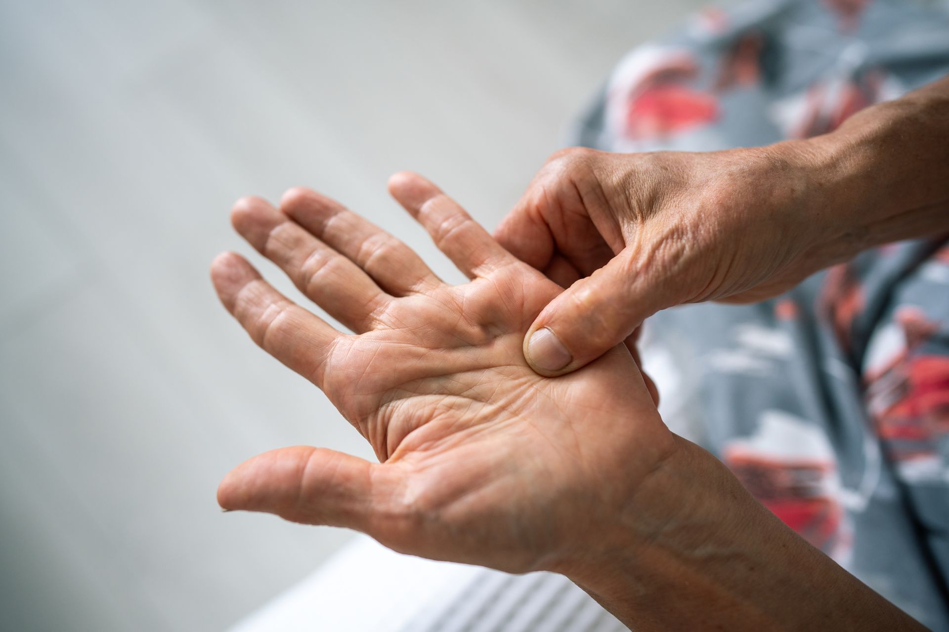 Person examines palm, pressing the base of the thumb. Hand has visible wrinkles.
