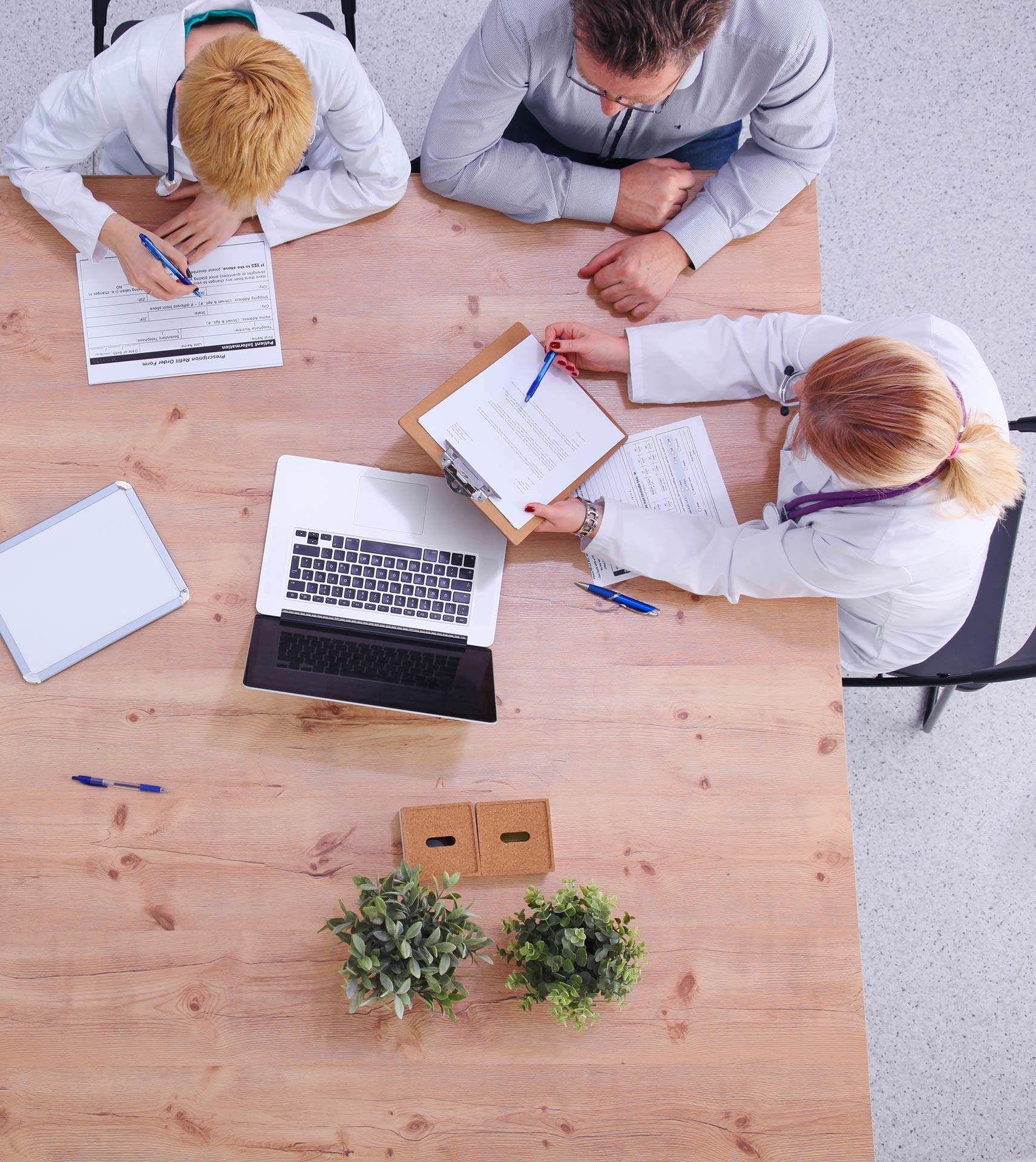 A group of doctors are sitting at a table with papers and a laptop.