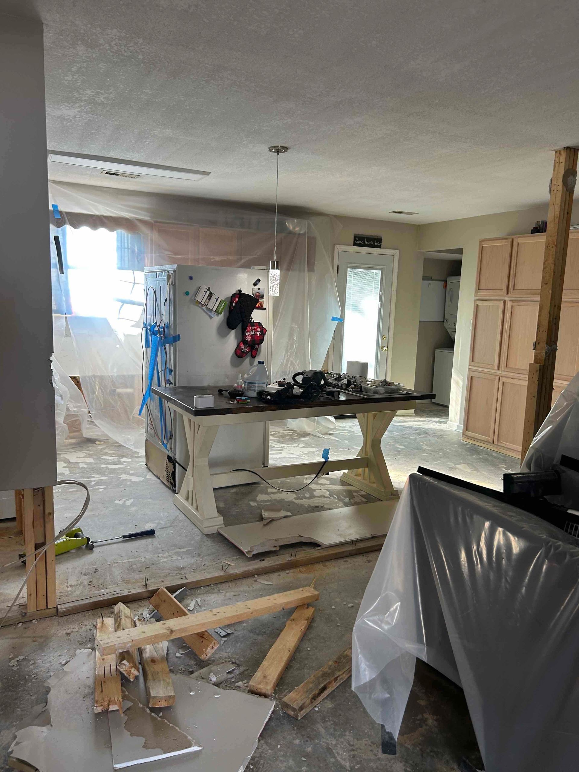 Kitchen undergoing renovation; island with dark countertop, cabinets, tools, and plastic sheeting.