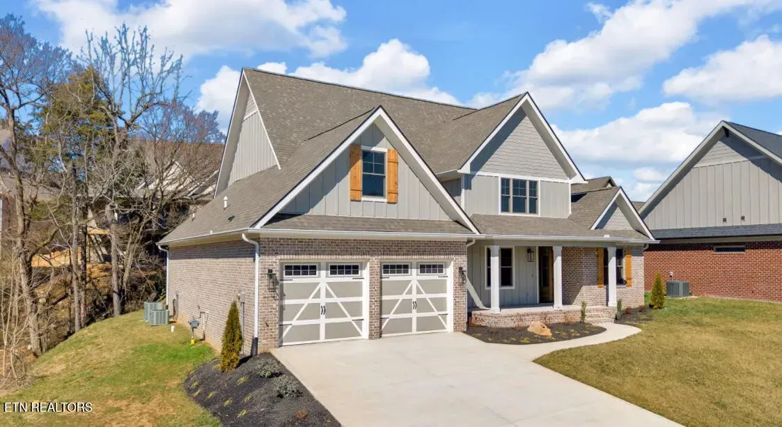 Gray two-story house with a brick facade and a two-car garage under a blue sky.