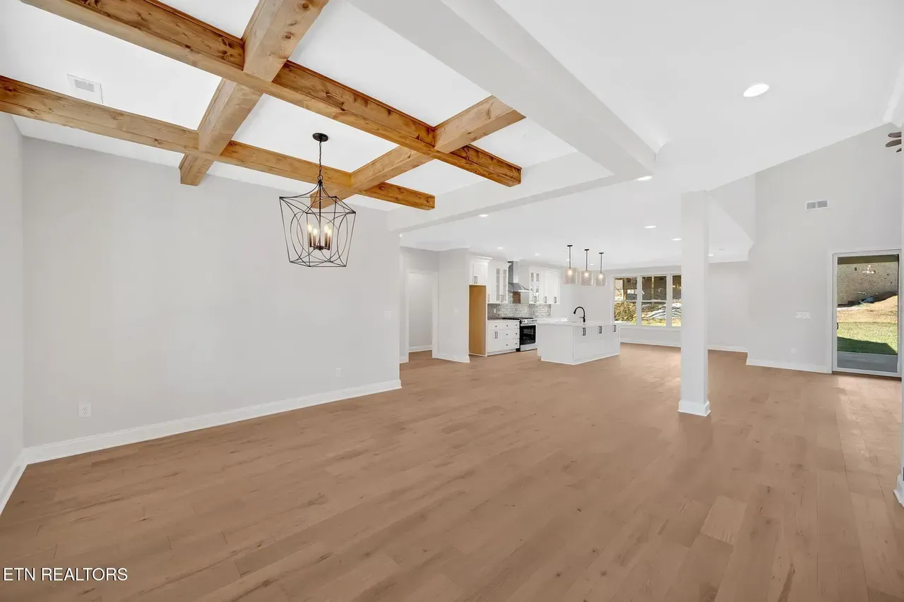 Spacious interior with wood beams, light wood floors, and white walls. Kitchen visible in the background.