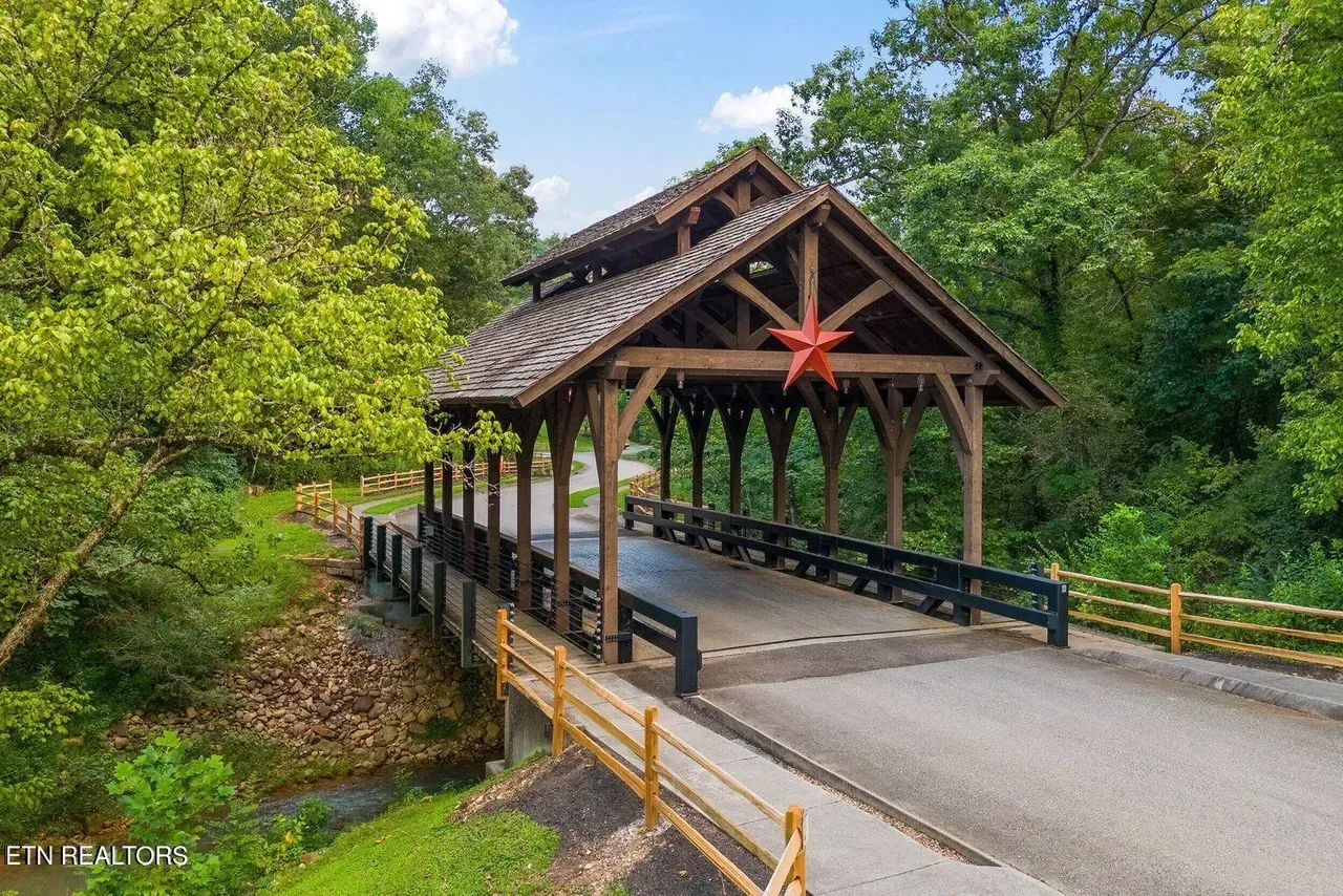 Covered wooden bridge with a red star decoration, surrounded by trees and a wooden fence.