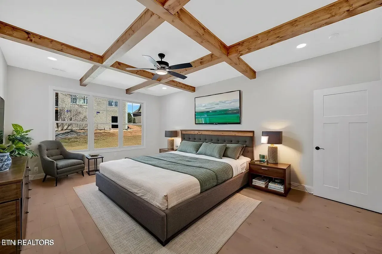 Bedroom with a bed, wood beams, and a sitting area by windows.