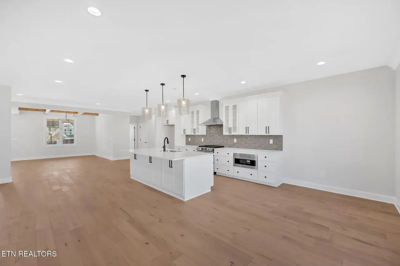 Modern open-concept kitchen with white cabinetry, island, and stainless steel appliances; light wood flooring.