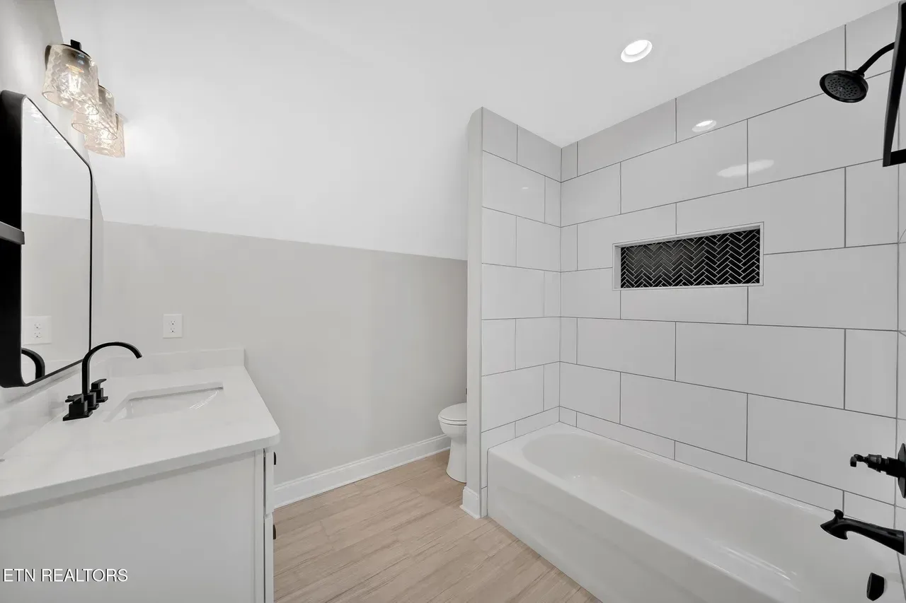 Bathroom with white walls, tub, and vanity; light wood-look floor, black fixtures.