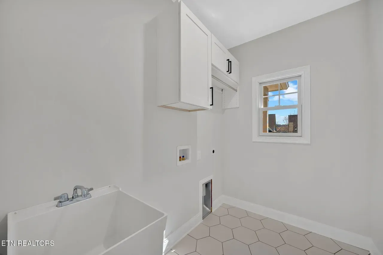 Laundry room with white cabinets, utility sink, and a small window.