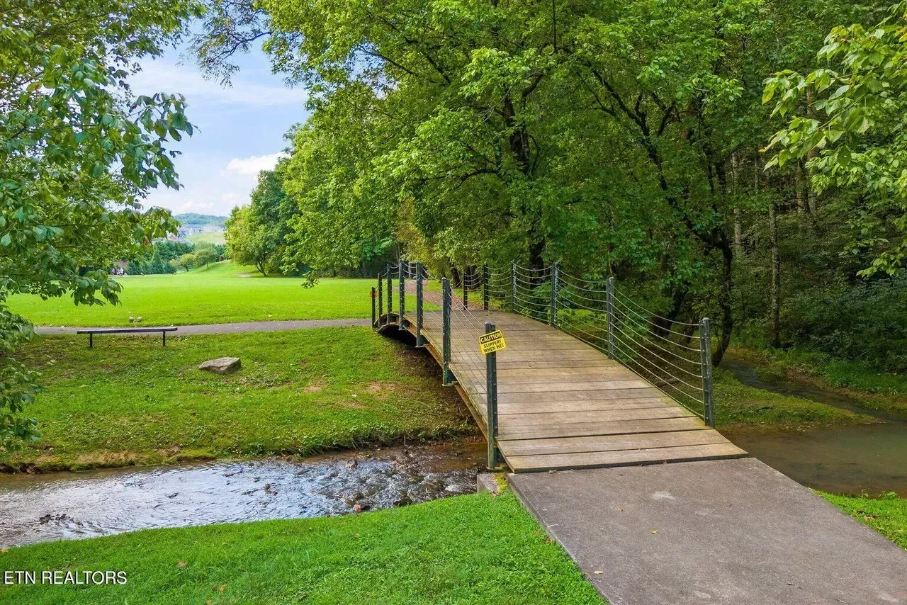 Wooden bridge over a creek in a park with green grass and trees.