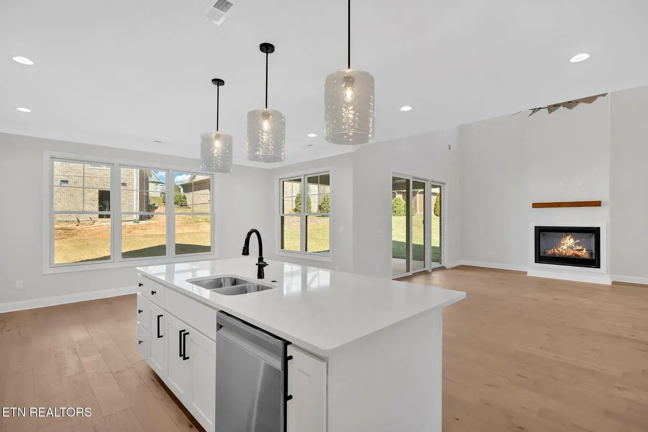 Modern kitchen with island, pendant lights, fireplace, and large windows.