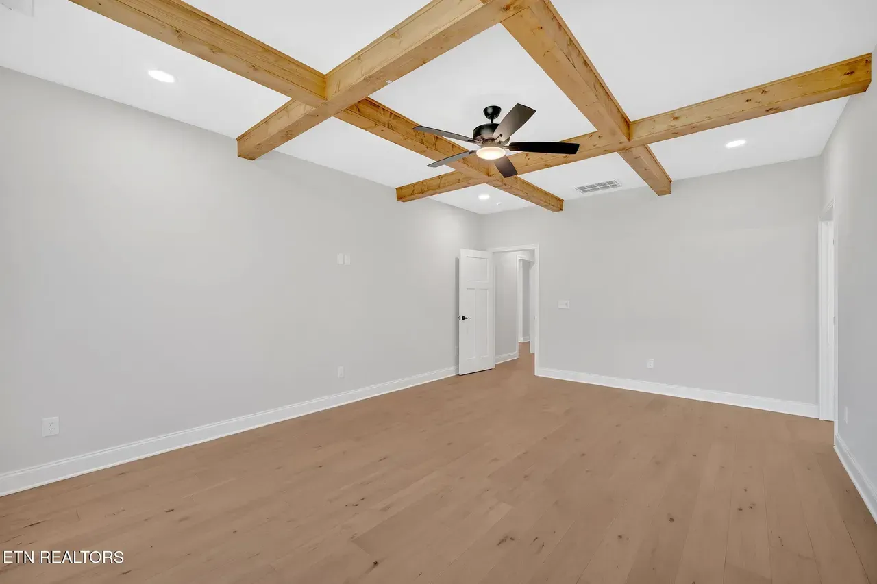 Empty room with wooden beams on the ceiling, light wood floor, and white walls.