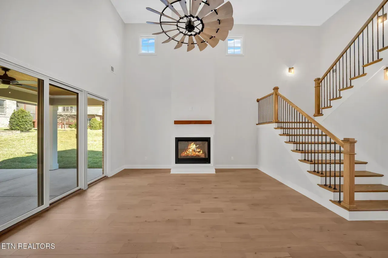 Empty living room with fireplace, stairs, sliding glass doors, and light wood floors.