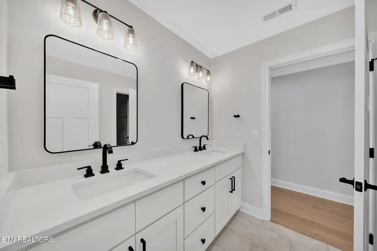 White bathroom with double vanity, black fixtures, and a doorway.
