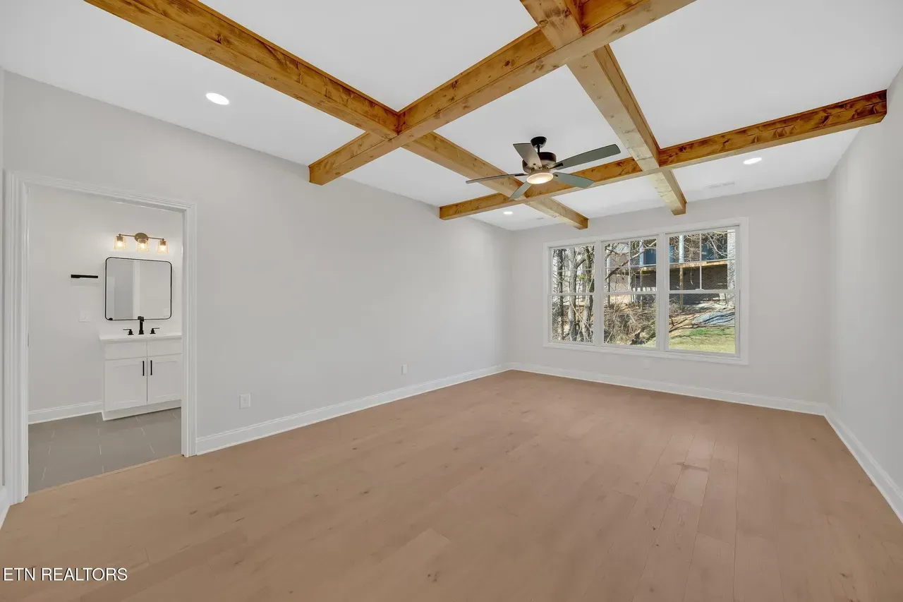 Spacious bedroom with wood beams on ceiling, light wood floor, and doorway to bathroom.