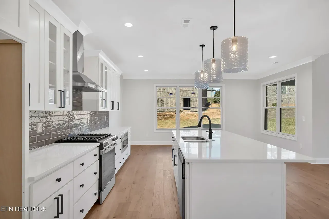 Modern white kitchen with stainless steel appliances, island, and wood floors.