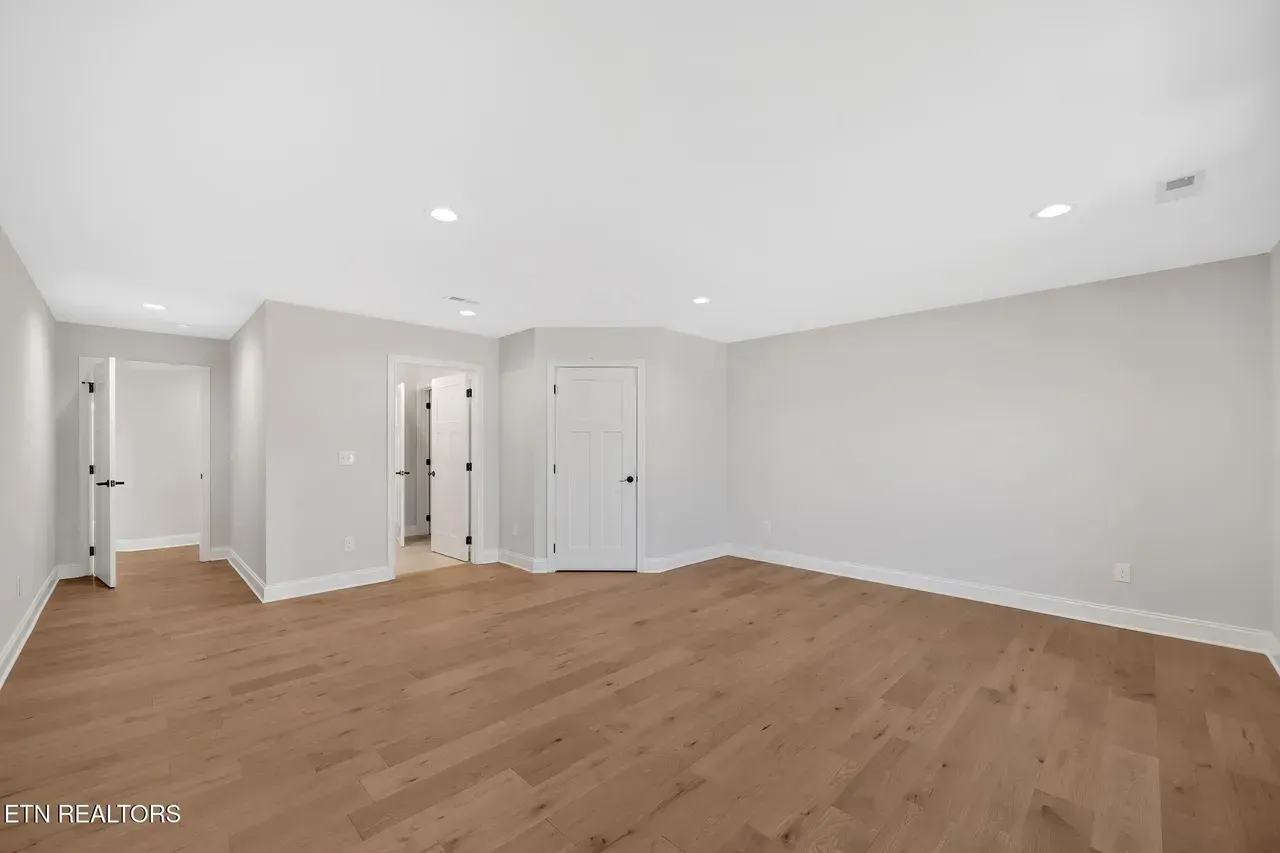 Empty room with wood floors, white walls, and three doorways.